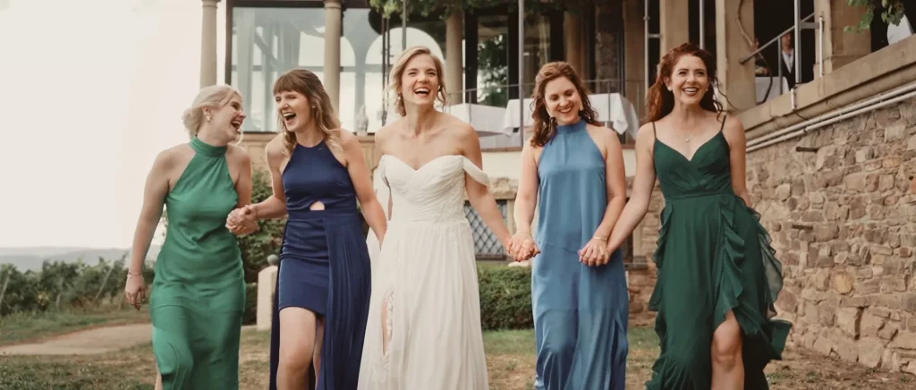 Eine Braut läuft Hand in Hand mit ihren 4 Brautjungfern auf die Kamera zu, während alle herzhaft lachen.